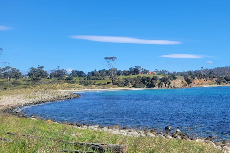 A blue water bay sorrounded by green bush is seen under a sunny sky.
