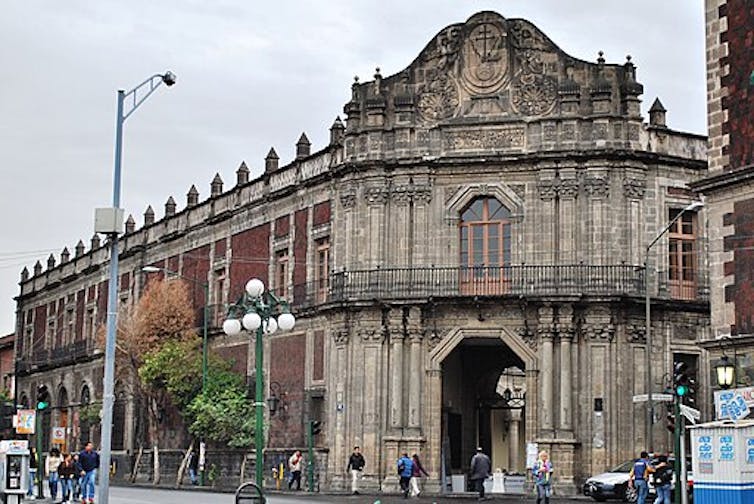 The stone and brick facade of an old, two-story building on a street with tall streetlamps.