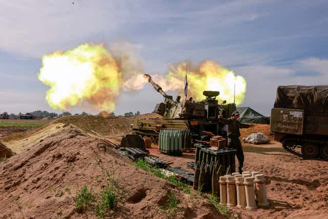A large armored gun releases a cloud of smoke, while a soldier gestures near racks of ammunition.