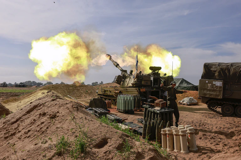 A large armored gun releases a cloud of smoke, while a soldier gestures near racks of ammunition.
