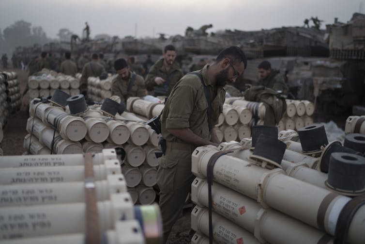Soldiers stand near piles of cylinders.