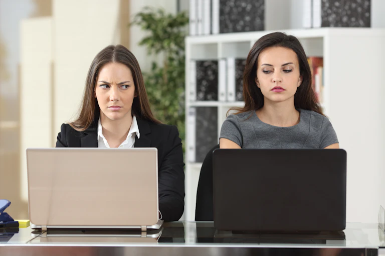 Two women sitting side-by-side and shooting one another rude looks