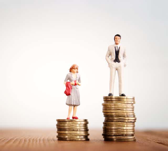 A figurine of a woman standing on a stack of coins next to a figurine of a man standing on a larger stack of coins