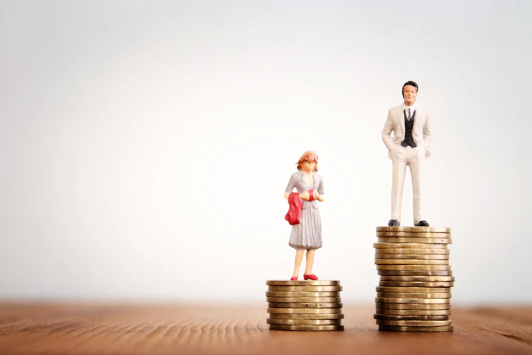 A figurine of a woman standing on a stack of coins next to a figurine of a man standing on a larger stack of coins