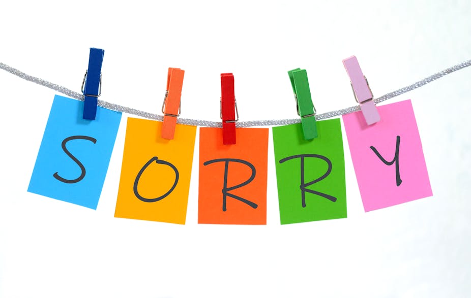 The word "sorry" is spelled out five different colored sticky notes hanging from clothespins of similar colors.