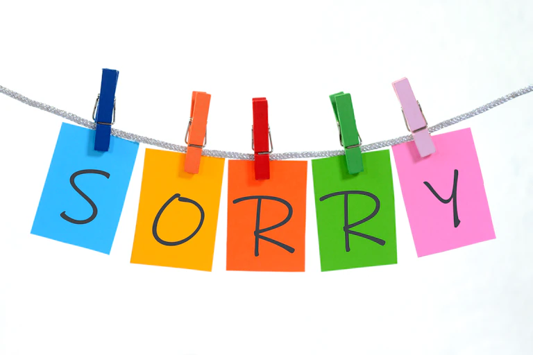 The word "sorry" is spelled out five different colored sticky notes hanging from clothespins of similar colors.