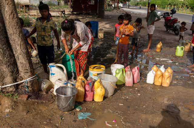 Informal settlement residents fill plastic containers with water in India