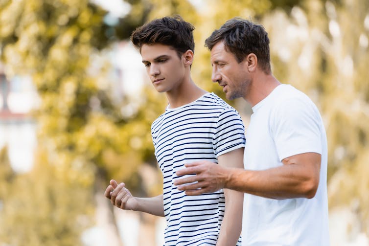 A teenage boy talking with a man outdoors.