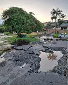 An ordinary urban road full of deep cracks, breaking tar and deep potholes filled with rain after being destroyed by floods