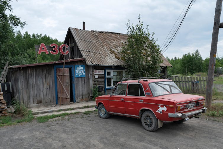 A red car parked outside an old wooden gas station.