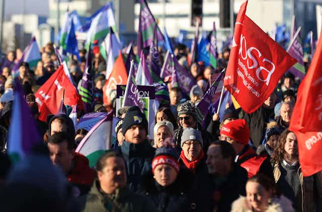 Crowd of workers in winter hats and coats, carrying flags representing public sector unions