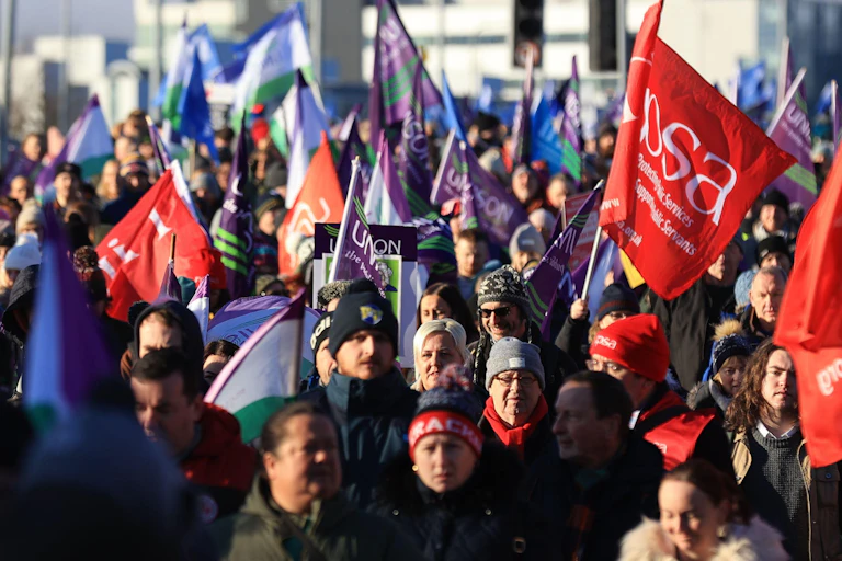 Crowd of workers in winter hats and coats, carrying flags representing public sector unions