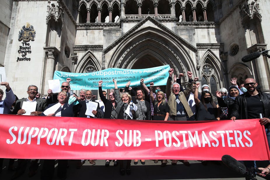 A group of people cheering outside the Royal Courts of Justice, carrying a large red banner reading Support our Sub-Postmasters