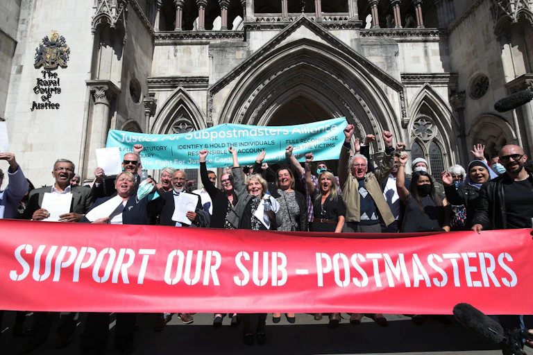 A group of people cheering outside the Royal Courts of Justice, carrying a large red banner reading Support our Sub-Postmasters