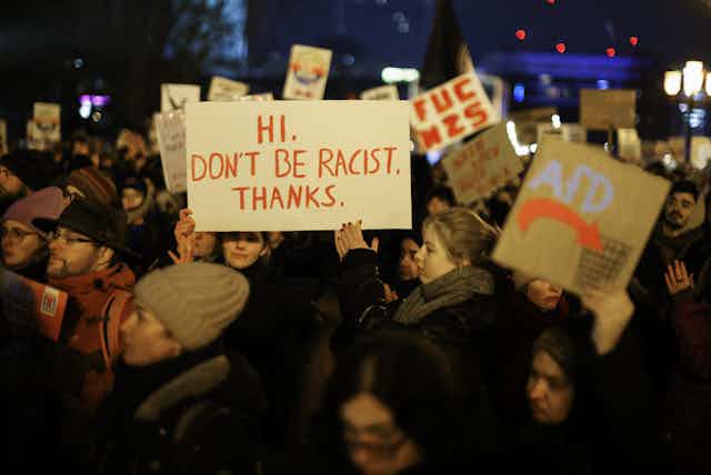 Des personnes brandissent des pancartes proclamant notamment « Hi. Don't be racist. Thanks. »