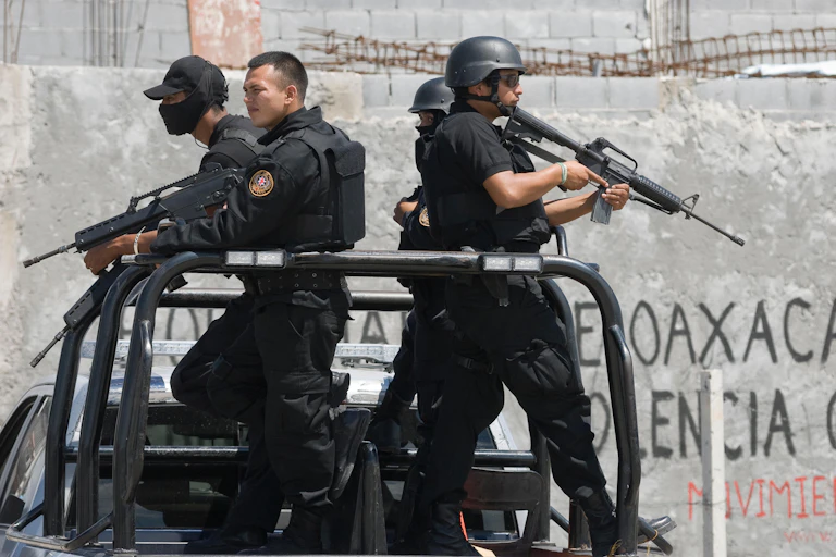 Four armed policeman standing on the back of a pick-up truck.