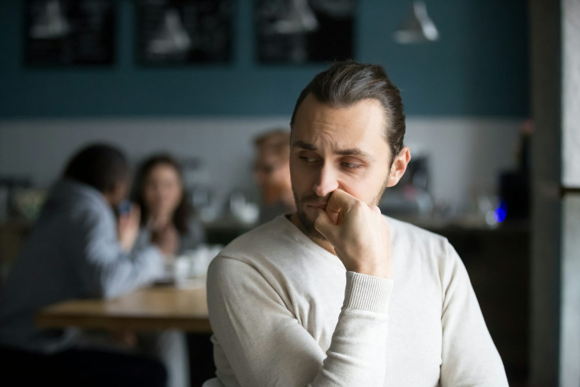 A man stands in the foreground looking over his shoulder while a group of people sit together at a table behind him