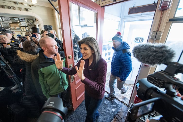 Nikki Haley cruza una puerta, saludando con ambas manos a una multitud de personas.  Varias cámaras de vídeo y teléfonos la apuntan de cerca.