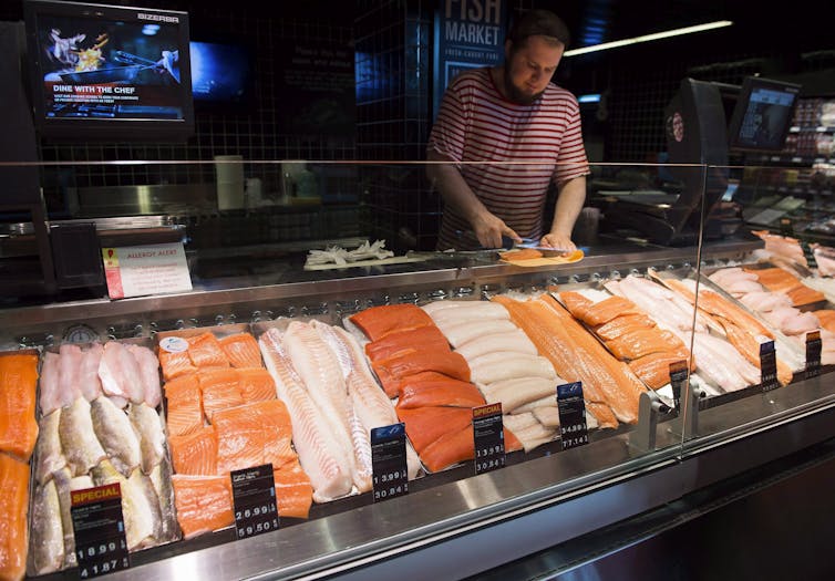 A man slicing fish behind a seafood counter in a grocery store displaying fresh fish