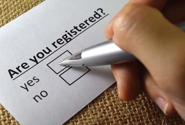 A person ticking a 'yes' box on a form that asks 'are you registered?'