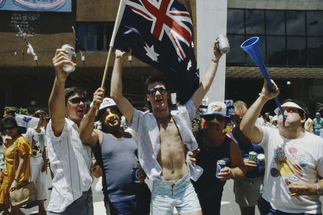 Male revellers drinking beer and holding the Australian flag in the 1980s