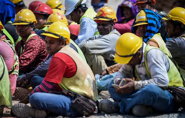 Workers wearing hardhats sitting on the ground