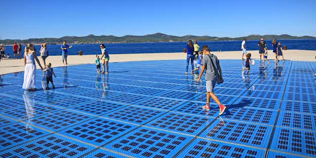 Families walk over blue solar panel paving on a sunny day.