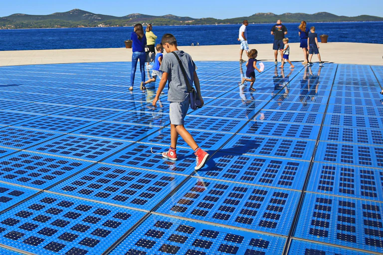 Families walk over blue solar panel paving on a sunny day.