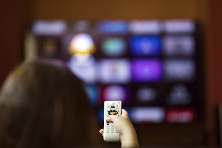 hand holding remote points at TV with many blurry app icons