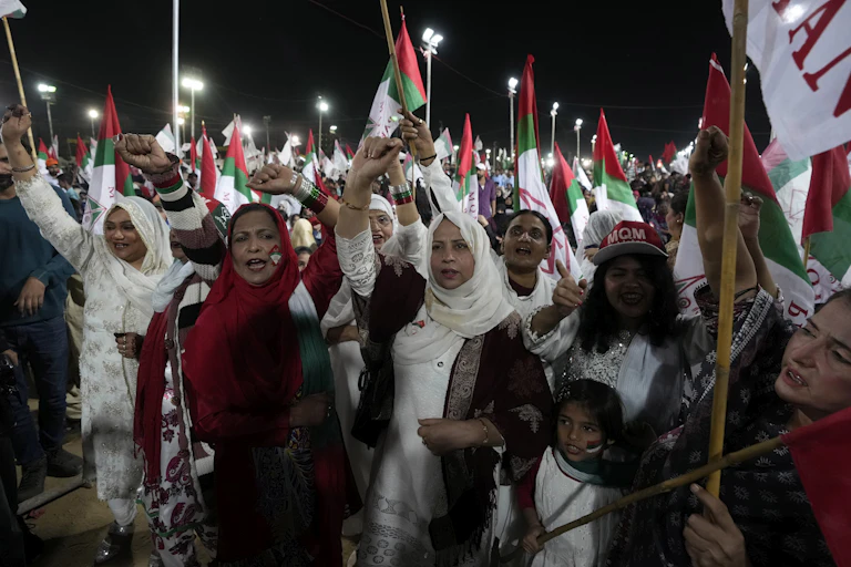 Pakistanis, mostly women, march and wave flags at a rally.