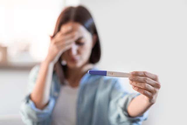 Woman looking at pregnancy test, holding her head