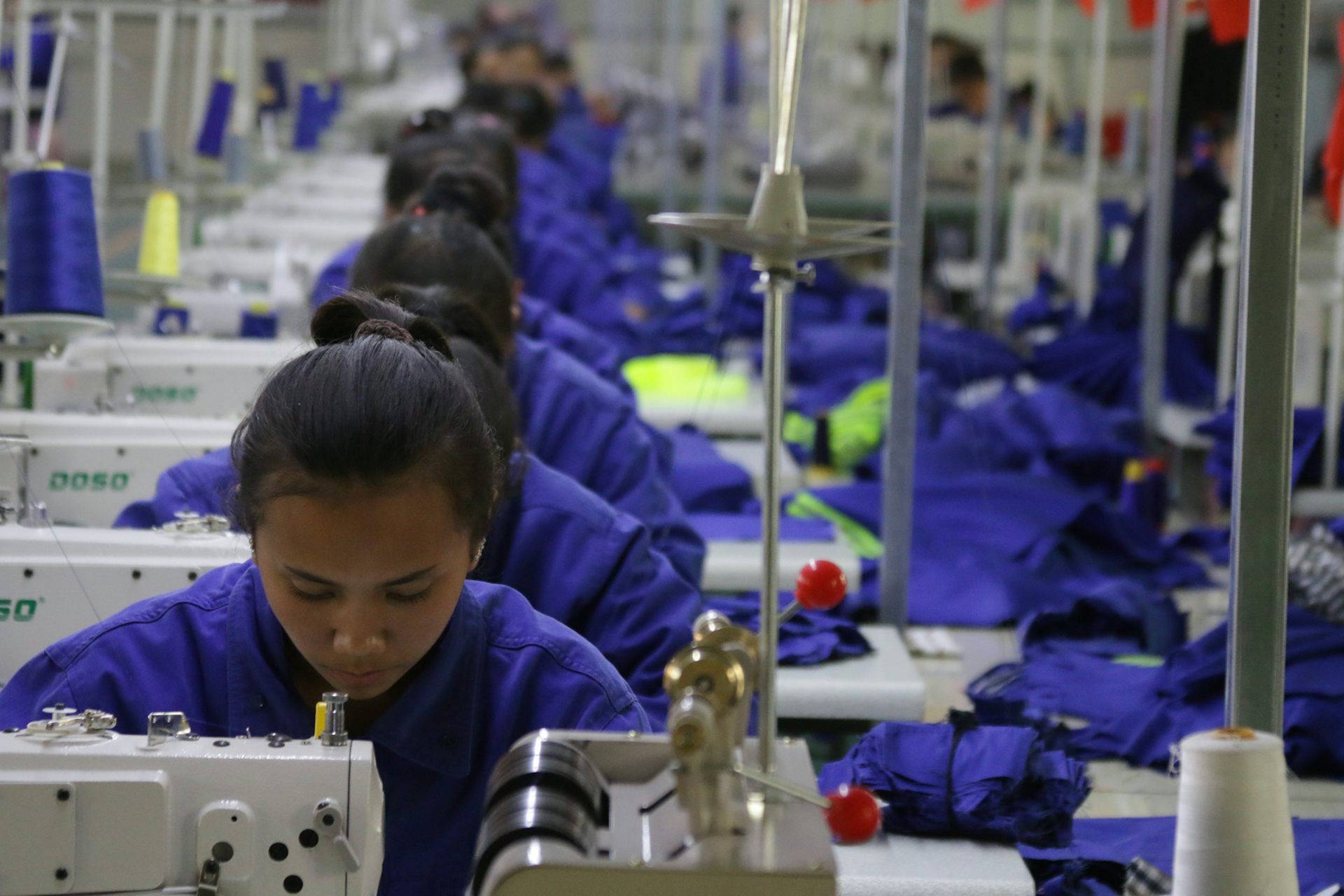 A line of women dressed in blue working at sewing machines.