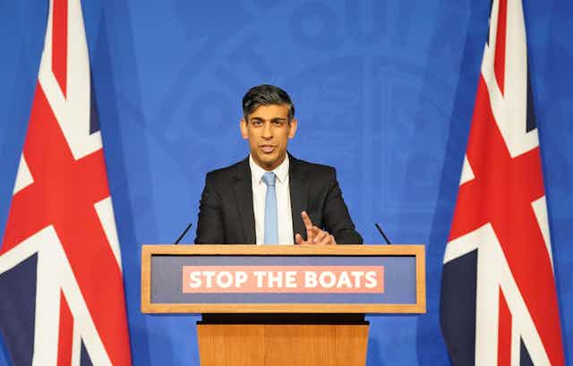 Rishi Sunak at a podium that reads Stop the Boats