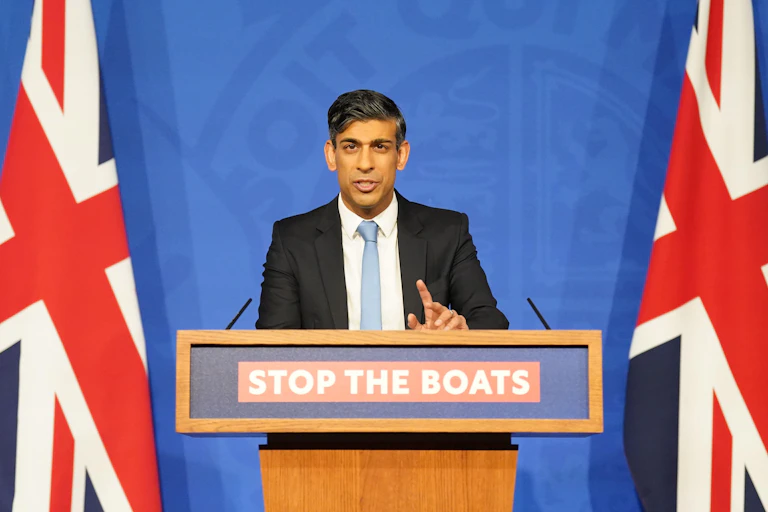 Rishi Sunak at a podium that reads Stop the Boats