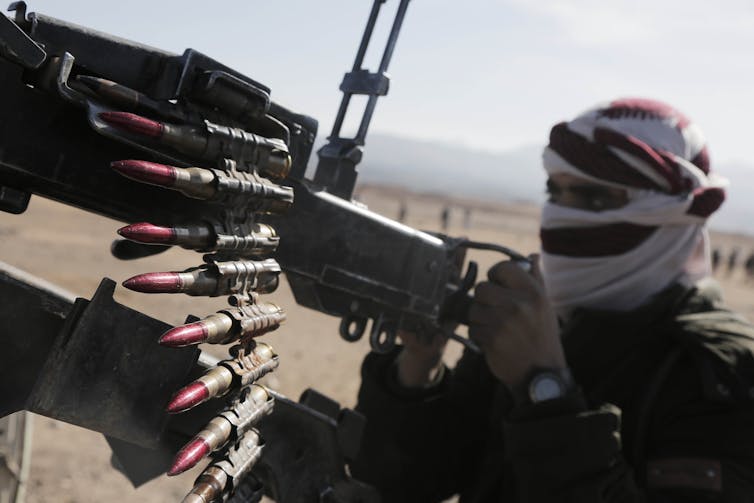 A man in a headscarf stands next to a heavy weapon with shells.