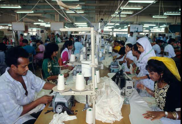 A group of people sat side-by-side at sewing machines in a factory.