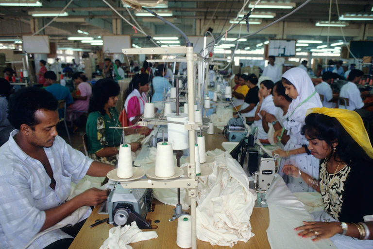 A group of people sat side-by-side at sewing machines in a factory.