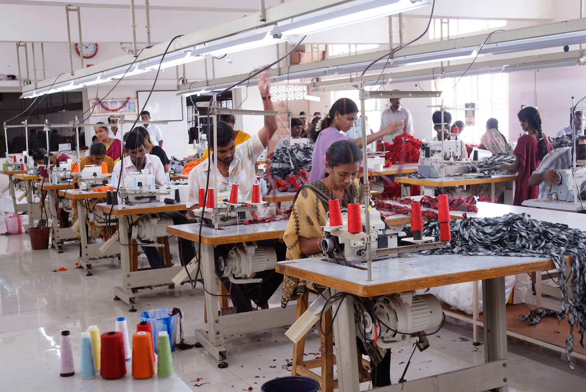Two rows of workers using sewing machines to stitch garments in a factory.