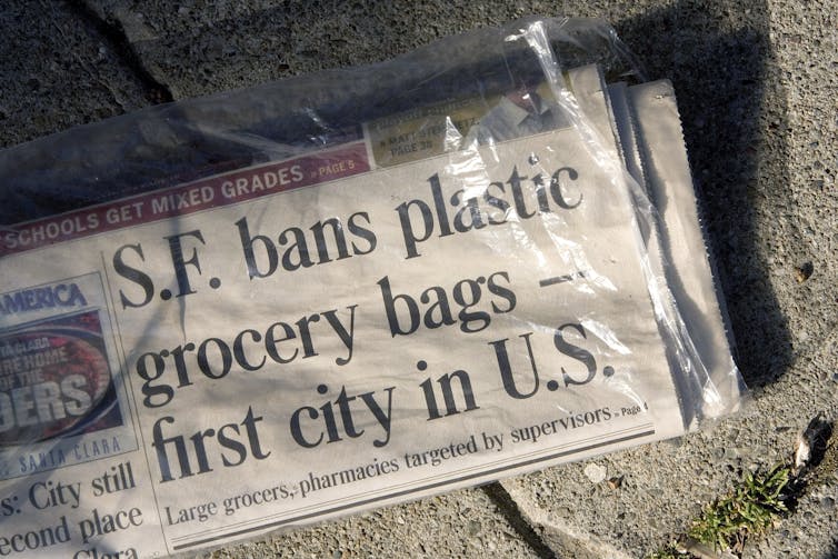 Newspaper in a plastic bag sitting on concrete. The headline on the newpaper reads ,"S.F. bans plastic grocery bags -- first city in U.S."