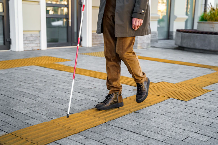 a man with a cane walks along a sidewalk with textured yellow surfaces