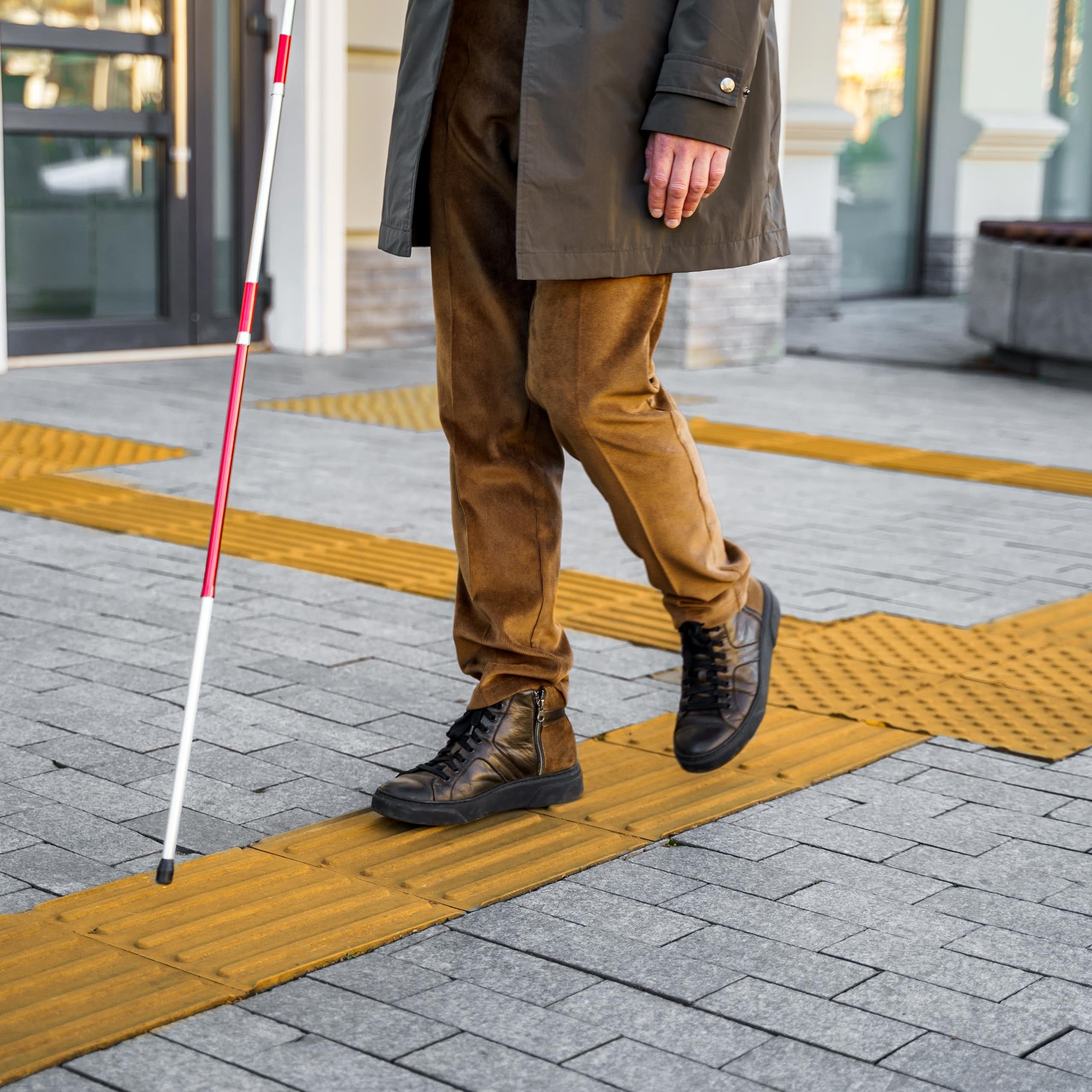 a man with a cane walks along a sidewalk with textured yellow surfaces
