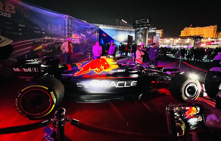 A black, futuristic-looking race car sporting the Red Bull logo is seen behind a velvet rope.