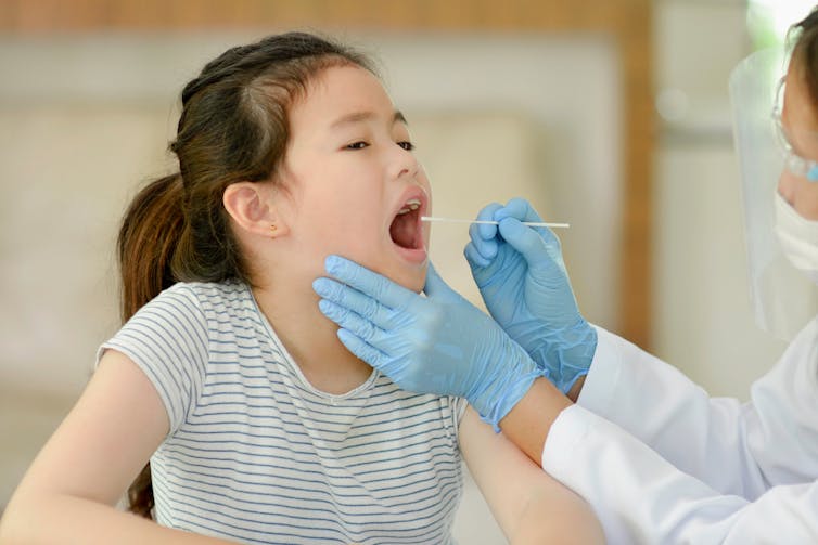A health professional out of frame swabbing a girl's throat