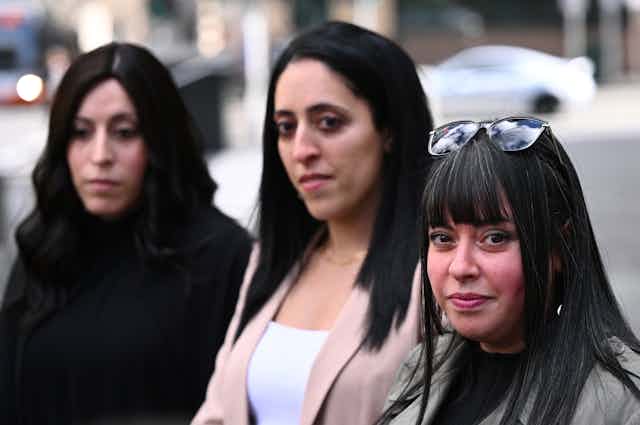 the three Erlich sisters stand in front of the County Court in Melbourne, with Dassi Erlich at front and most sharply in focus