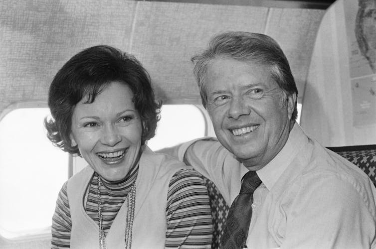 A black and white historical photo of a smiling Jimmy and Rosalynn Carter on board their campaign plane.