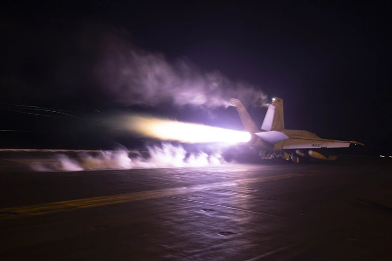 An aircraft carrier with a plume of flame jutting from its rear.
