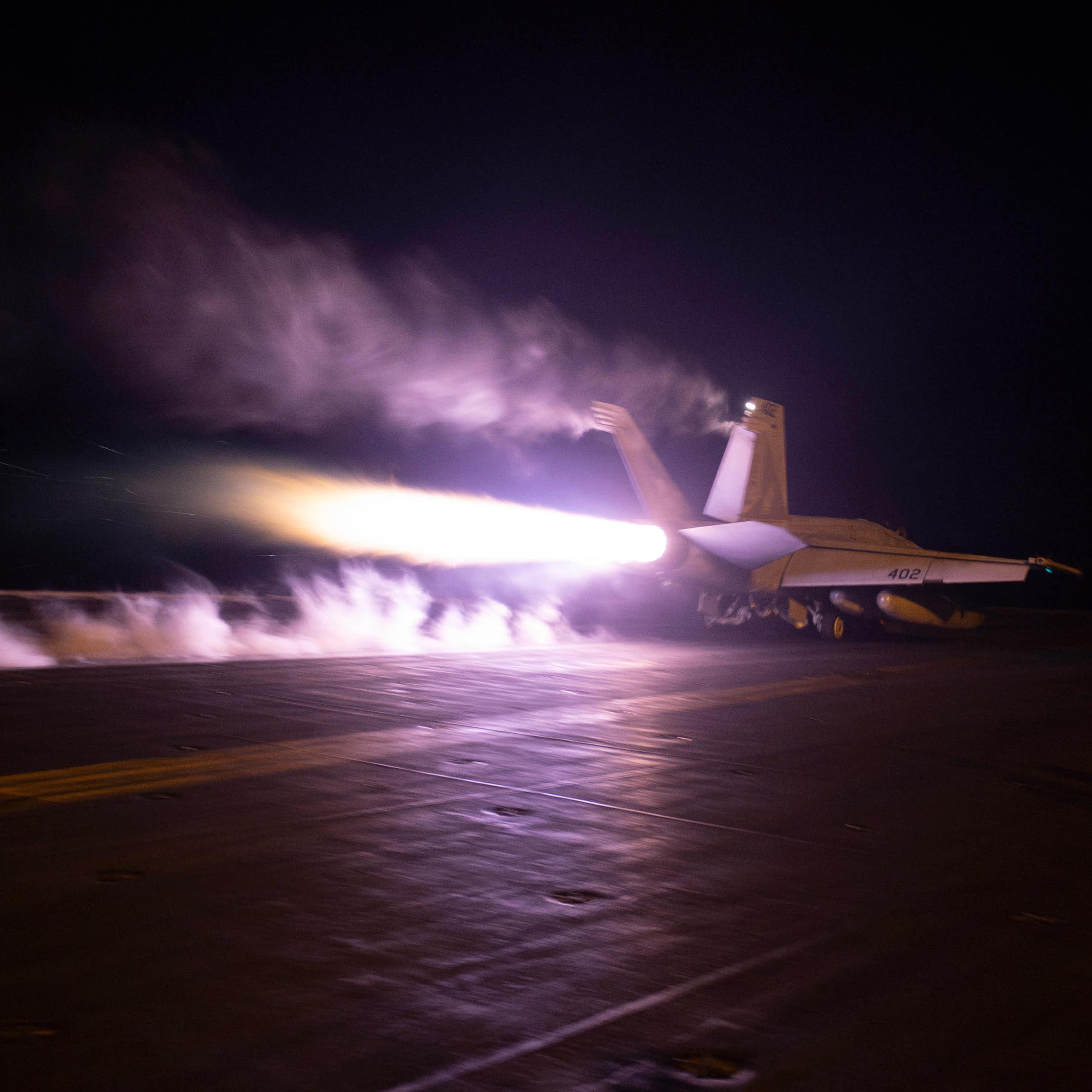 An aircraft carrier with a plume of flame jutting from its rear.