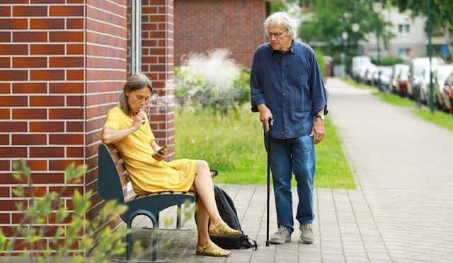 Older woman vapes on bench, her elderly friend looks on