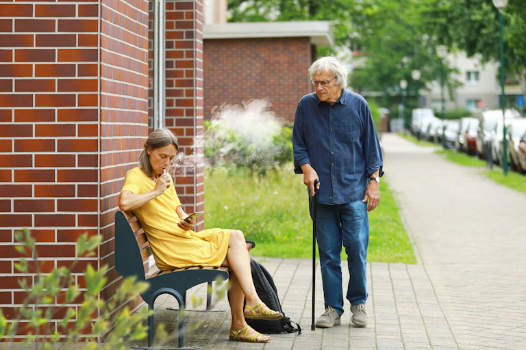 Older woman vapes on bench, her elderly friend looks on