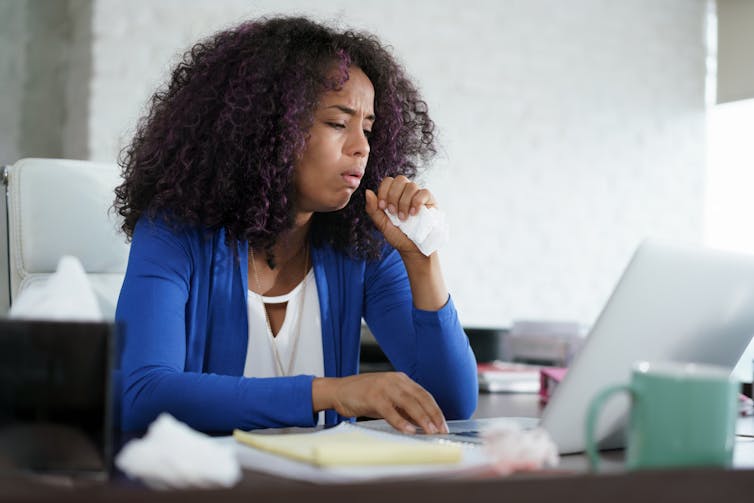 A woman coughing at her desk.